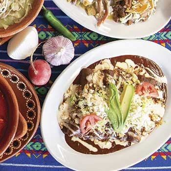 Enchiladas con crema, queso, aguacate y jitomate sobre un sarape