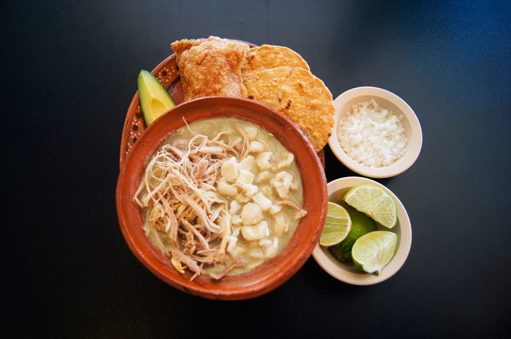 Pozole blanco en cazuela de barro con tostada, aguacate, limón y cebolla